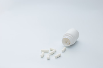 A lonely white bottle lies on a white background, several white capsules spilled from a white bottle