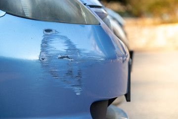 Scratch on a bumper of a blue car on a public parking. Not a rare scene in urban parking...