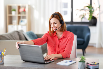 remote job, technology and people concept - happy smiling young woman with headset and laptop computer having video conference at home office