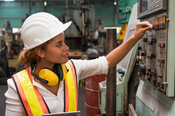 Female industrial worker working and checking machine in a large industrial factory with many equipment.