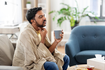people, healthcare and problem concept - sick man with cup of tea touching his sore throat at home