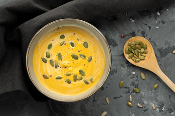 Creamy pumkin soup with seeds is ready on grey background with spoon and napkin. Top view