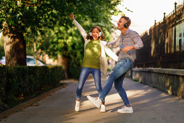 Happy young couple dancing on the street and listening to music through headphones