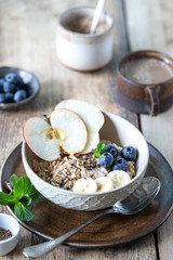 Healthy breakfast, oatmeal or granola with blueberries, apple, nuts and mint on a rustic wooden background