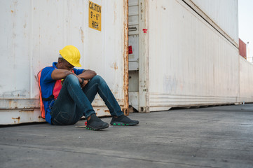 Tired  depressed black foreman worker working at Container cargo harbor to loading containers. African dock male staff fall asleep for Logistics import export shipping concept.