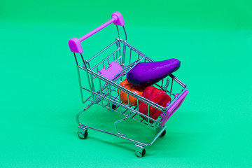 Toy vegetables in self-service shopping cart with pink handle isolated on green background. Top...