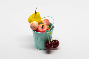 Colorful mini toy fruits in tiffany blue bucket isolated on white background. Pear, cherry, peach...
