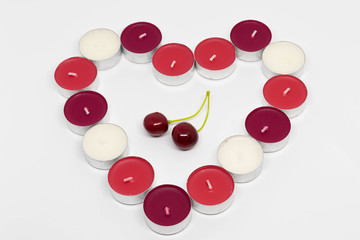 Heart shape formed by tea light candles with cherry in the middle. White and red candles forming heart shape isolated on white background. Love idea design concept