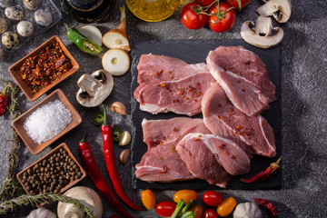 Pork steaks, fresh vegetables, spices close-up on a textured background top view