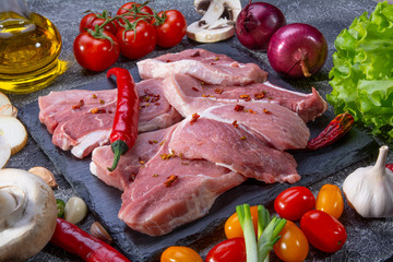 Pork steaks, fresh vegetables, spices close-up on a textured background top view
