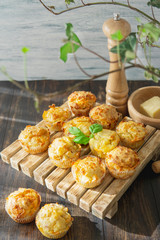 Homemade savory muffins with cheese, herbs on a wooden plate, dark background with green plants. Fresh baked,  healthy snack or breakfast meal. Natural light. 