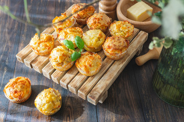 Homemade savory muffins with cheese, herbs on a wooden plate, dark background with green plants....