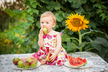 little girl of 10 months on the street in the yard in the summer in a colored dress there is a red...