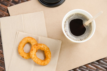 coffee in a paper cup next to onion rings on a paper napkin. Unhealthy fast food