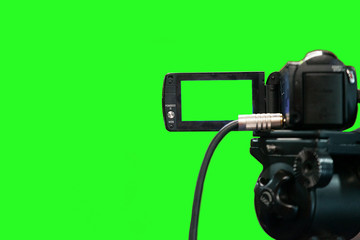 A video camera on a green background with a view from behind. Camera screen with green background