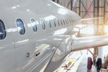 View of the fuselage of a passenger airliner with portholes and a wing with a landing gear in a repair hangar for aircraft.