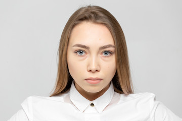 Close-up portrait of beautiful happy young attractive blonde woman in a white shirt with clean skin looking at camera against gray-white background