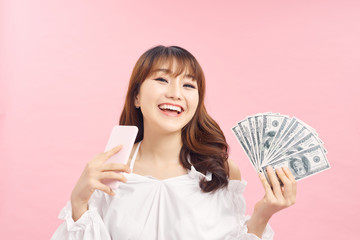 Image of a shocked surprised screaming young pretty woman posing isolated over pink wall background using mobile phone holding money.