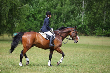 Young equestrian sports girl jumping obstacle with bay horse