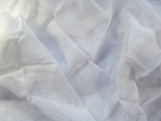 Medical gauze lies carelessly with folds on a white surface. Clean blank white mesh fabric pattern