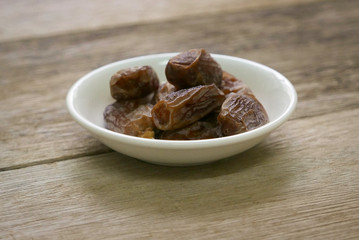 Selective focus of a dried dates fruit in a white bowl  on wooden background. Ramadan holy month for muslim concept where they are fasting.