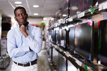 Positive man chooses TV set in store of household appliances