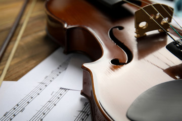 Beautiful violin, bow and note sheets on wooden table, closeup