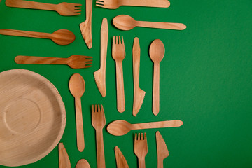 Eco-friendly disposable utensils made of bamboo wood on a green background. Draped spoons, fork, knives, bamboo bowls with