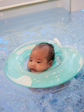 3 Months Little Asian Baby Girl Learning To Swim With Swimming Ring In An Indoor Pool, With Copy Space.