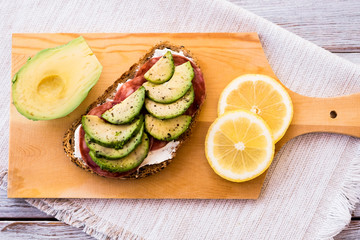 Fresh wholemeal sandwich with cheese, salami and avocado filling - on a wooden cutting board - diet and light lunch concept