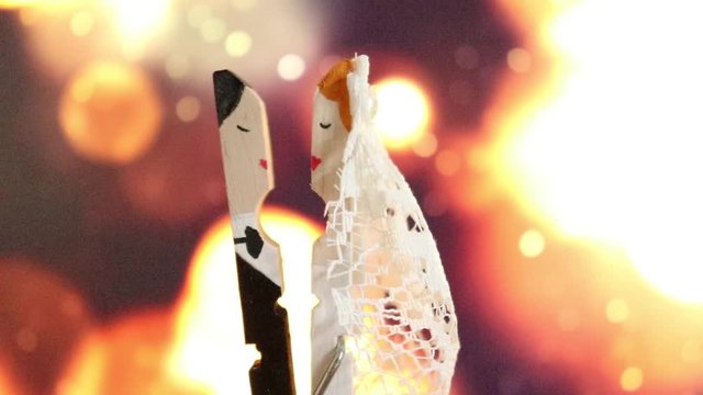 A clothespin hand painted as a groom and a bride kissing on the special day of their wedding on a bokeh defocused light background