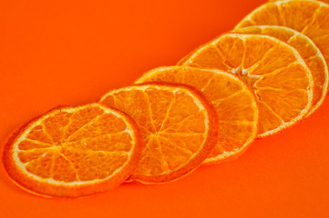Chips of dried tangerines, sliced in thin circles. Shot on an orange background. Background for vegetarianism and healthy eating.