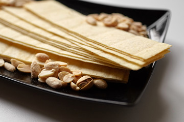 Beer snacks. Long potato chips, salted roasted peeled peanuts in black plate on white table