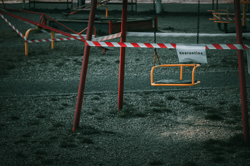 A children's swing on the playground is closed with a warning tape with a quarantine sign. Coronavirus, Covid-19 prohibition, restriction