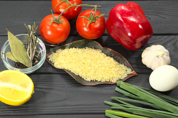 Raw rice and vegetables, ingredients for cooking. Chicken egg, vegetables and spices on a black wooden background.