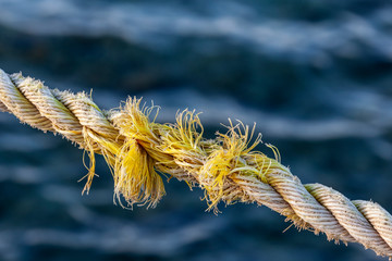 Frayed rope near to break on blue sea water background. Selective focus