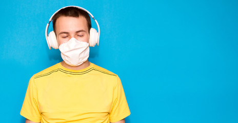 handsome serenity man with close eyes in medical mask and headphones listening to music isolated on blue background