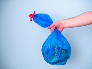 Men's hands holding used blue plastic garbage bag isolated on a blue background