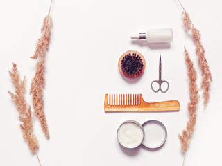 Accessories for the care of a beard and mustache are on a white background. Here are a wooden comb, a brush with stiff bristles, an open jar with balm or hair styling. Top view. lat lay.
