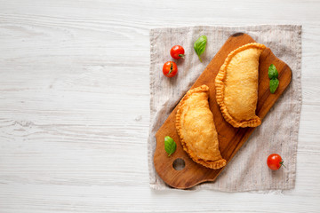 Homemade Deep Fried Italian Panzerotti Calzone on a rustic wooden board on a white wooden background, top view. Flat lay, overhead, from above. Copy space.