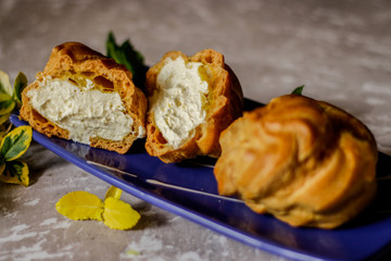 Delicious big cream puffs with cream in hand painted blue oval saucer with mint leaves on aged wooden background. Selective focus.