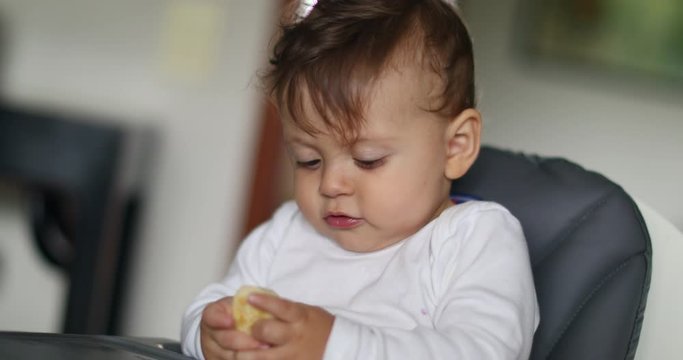 Cute baby boy eating pieces of banana seated on highchair