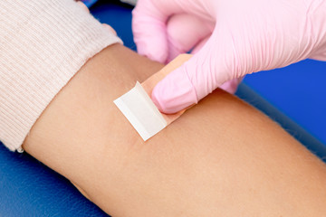 Nurse hand is glueing an adhesive plaster on arm after blood sampling,