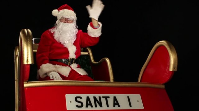 Santa Claus sat in his sleigh waving to the camera. Father Christmas on a black background. Stock Video Clip Footage
