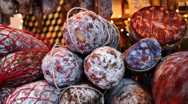 handmade sausages and salami, piled on top of each other, more sausages hanging in the background, charcuterie ingredients