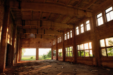 A large abandoned industrial building is lit by light from the windows. Large red brick building.