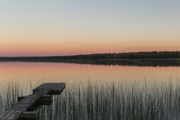 wooden jetty in a calm lake that looks like a mirror, in the background trees are reflected and the...