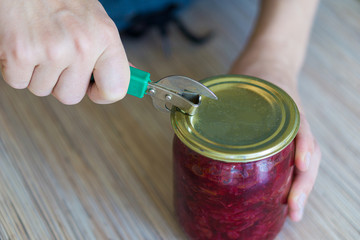 A woman in the kitchen opens a can of canned borscht with a hand-held can opener