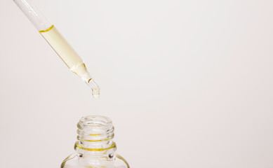 Cosmetic oil drips from a pipette into a glass jar. Oil for hair and skin. Spa treatments, skin and hair care.