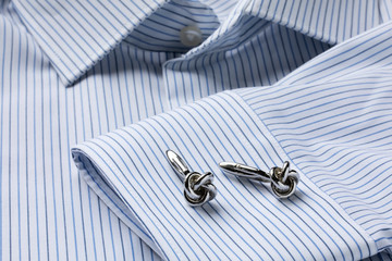 Fototapeta na wymiar Striped white and blue men's shirt close up with knot shape cufflinks. Close-up. Selecrive focus.